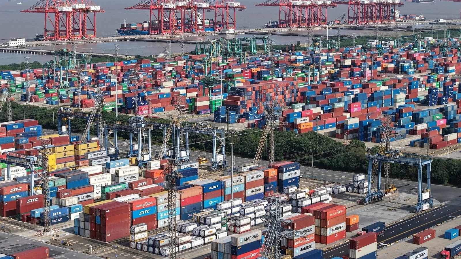An aerial view of a container terminal with rows of stacked shipping containers and gantry cranes at a port.