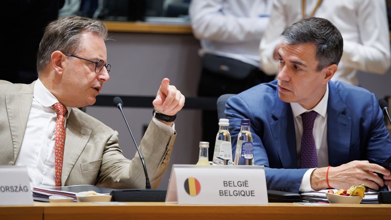 Two heads of government seated beside each other at a European Council table, one gesturing towards the other, behind a nameplate reading Belgie Belgique.