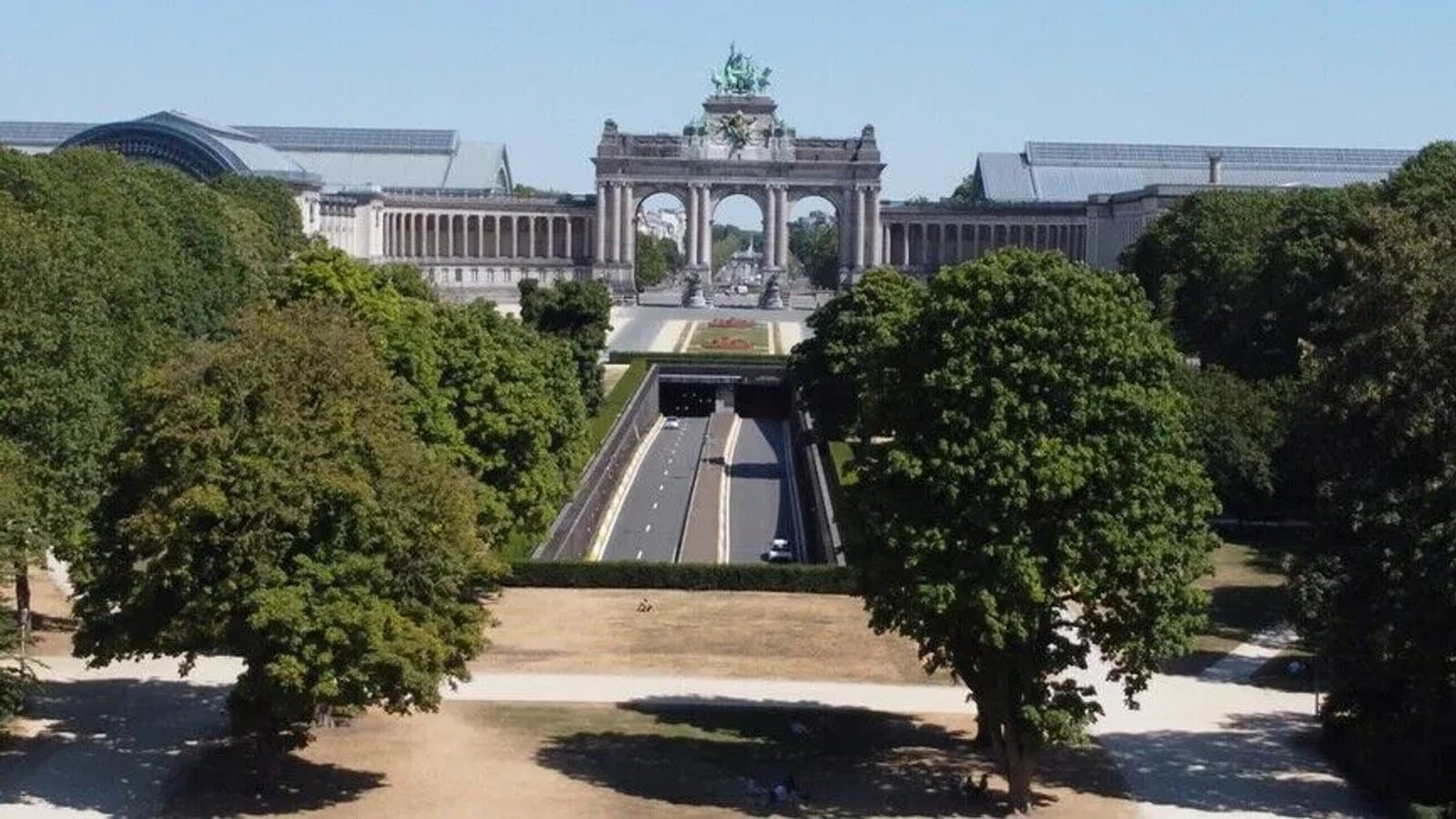 The Cinquantenaire Park in Brussels seen from above, its wide central lawn browned by drought with the triumphal arch and the tunnel road beyond.