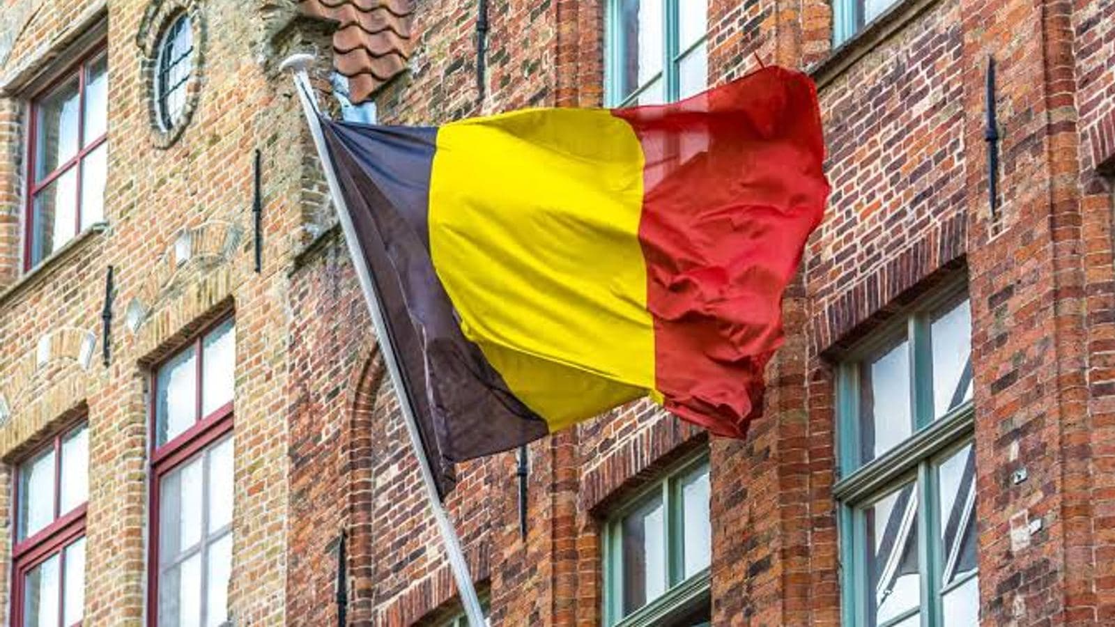 The Belgian tricolour flying from a pole on the brick facade of an old town house.