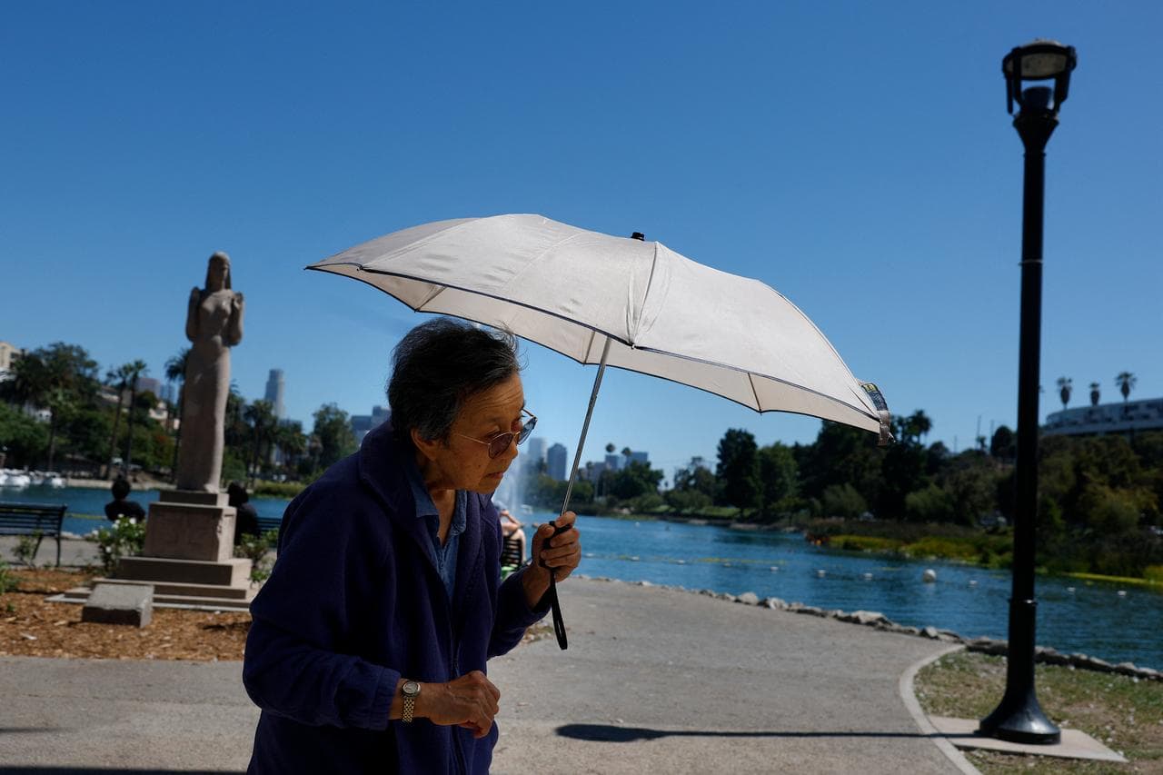 An elderly woman shields herself from the sun with an umbrella on a hot day