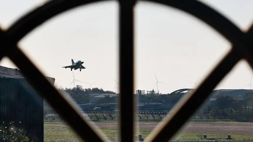A fighter jet taking off near wind turbines, seen through a round window frame