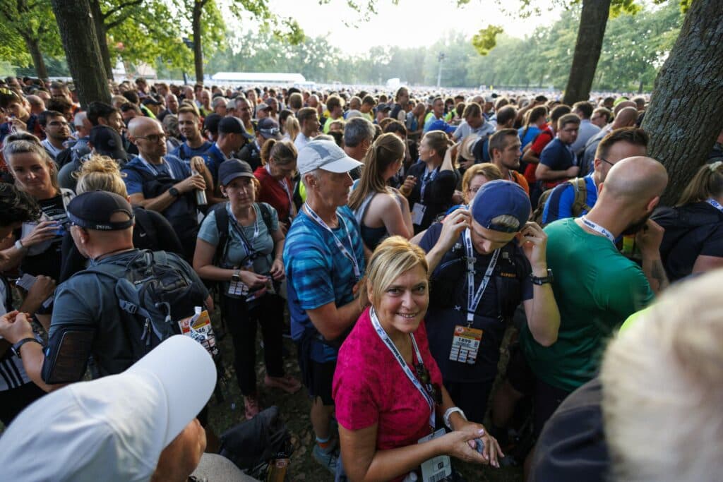 A dense crowd of hikers wearing backpacks and event lanyards gathered under trees at the start of the Dodentocht