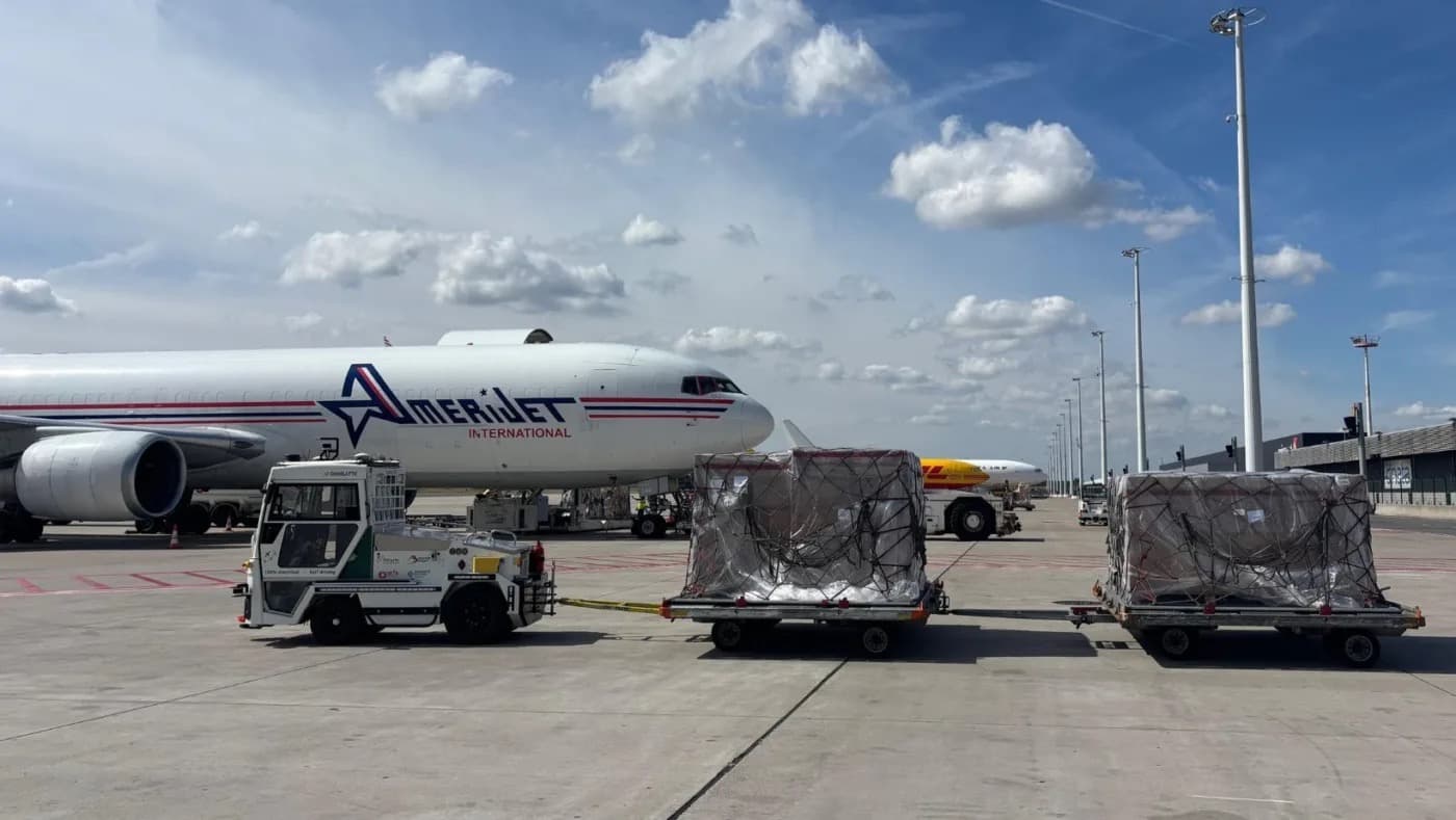 A cargo tow tractor pulling loaded trailers across the tarmac in front of a freighter aircraft