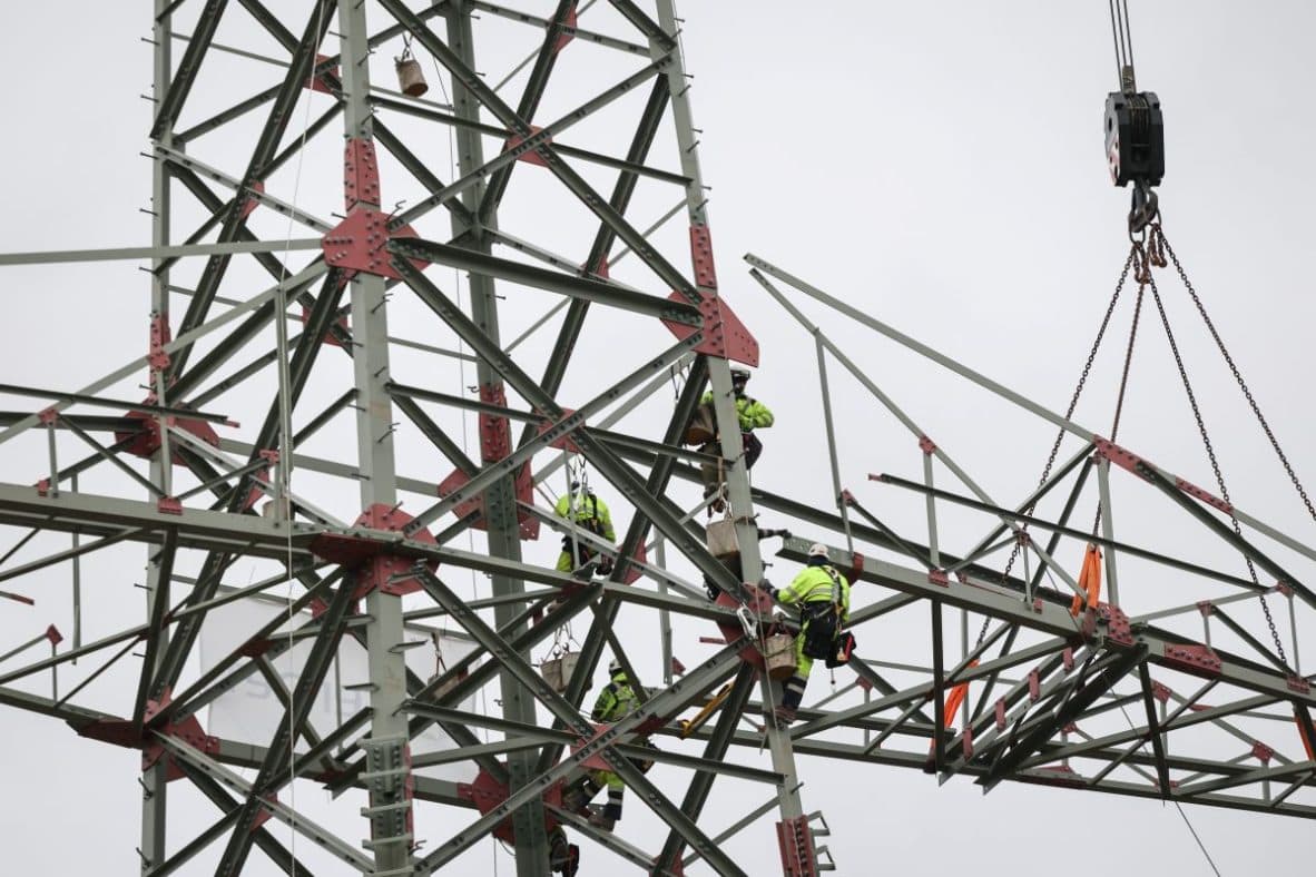 Workers in safety gear assembling a high voltage electricity pylon with a crane