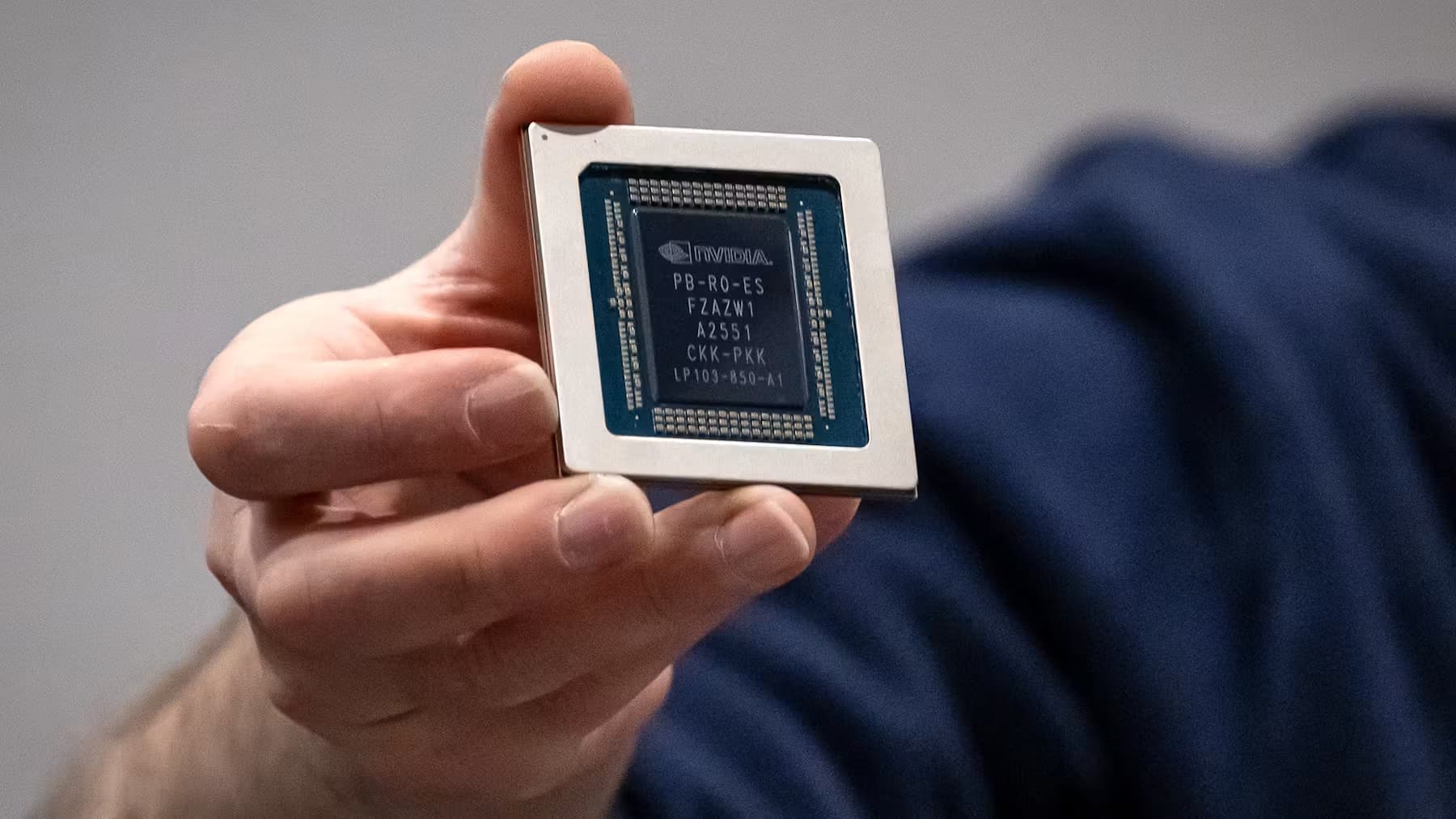 A hand holding a large AI computer chip stamped with the Nvidia logo