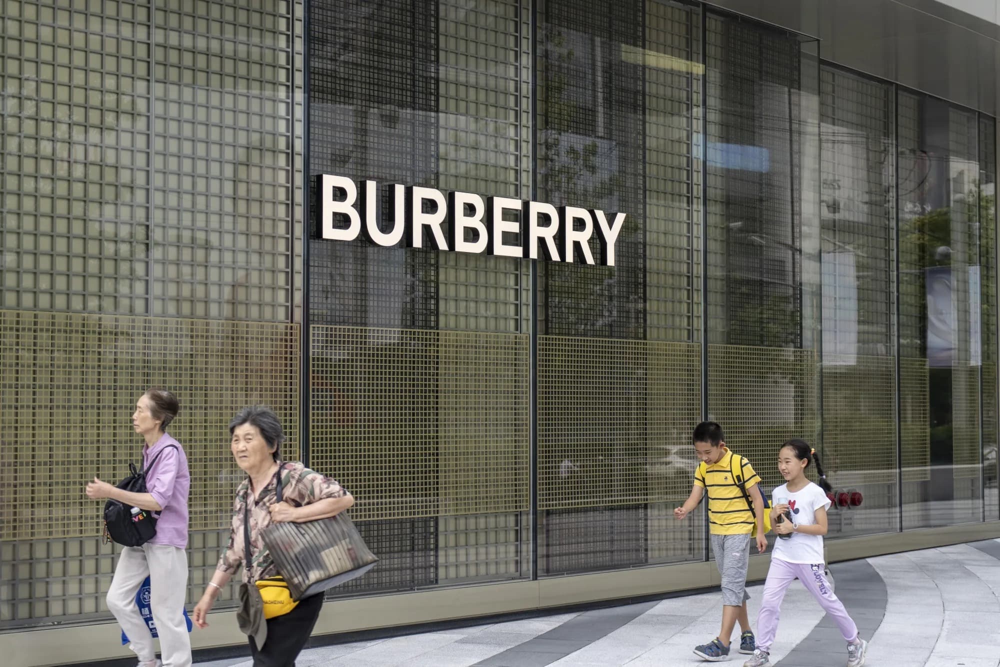Pedestrians and children walking past a Burberry storefront with a large illuminated logo