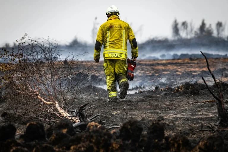 A firefighter in yellow protective gear walking across scorched, smoldering ground in the High Fens