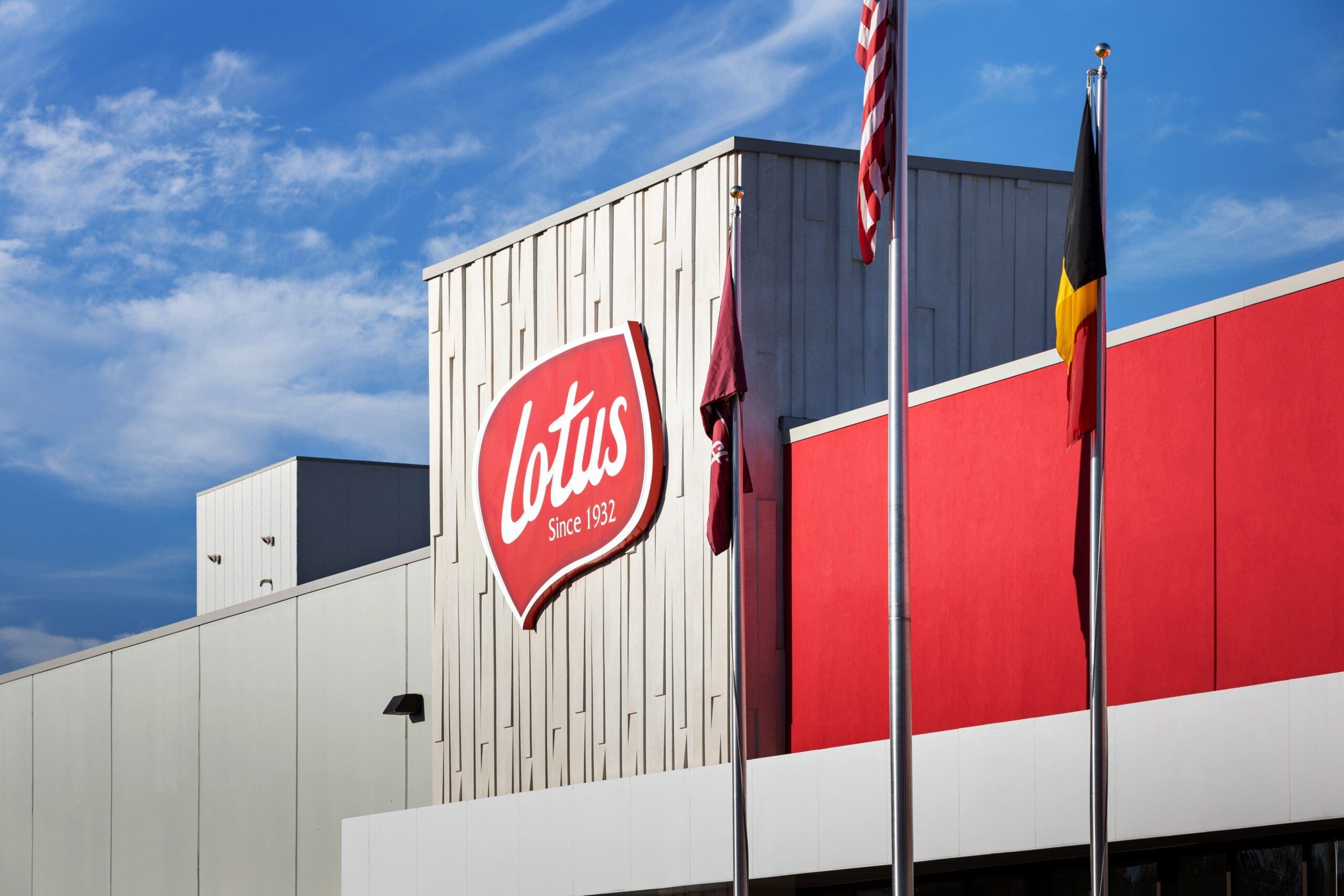 The Lotus company logo mounted on the exterior of a factory building, with the American and Belgian flags flying nearby