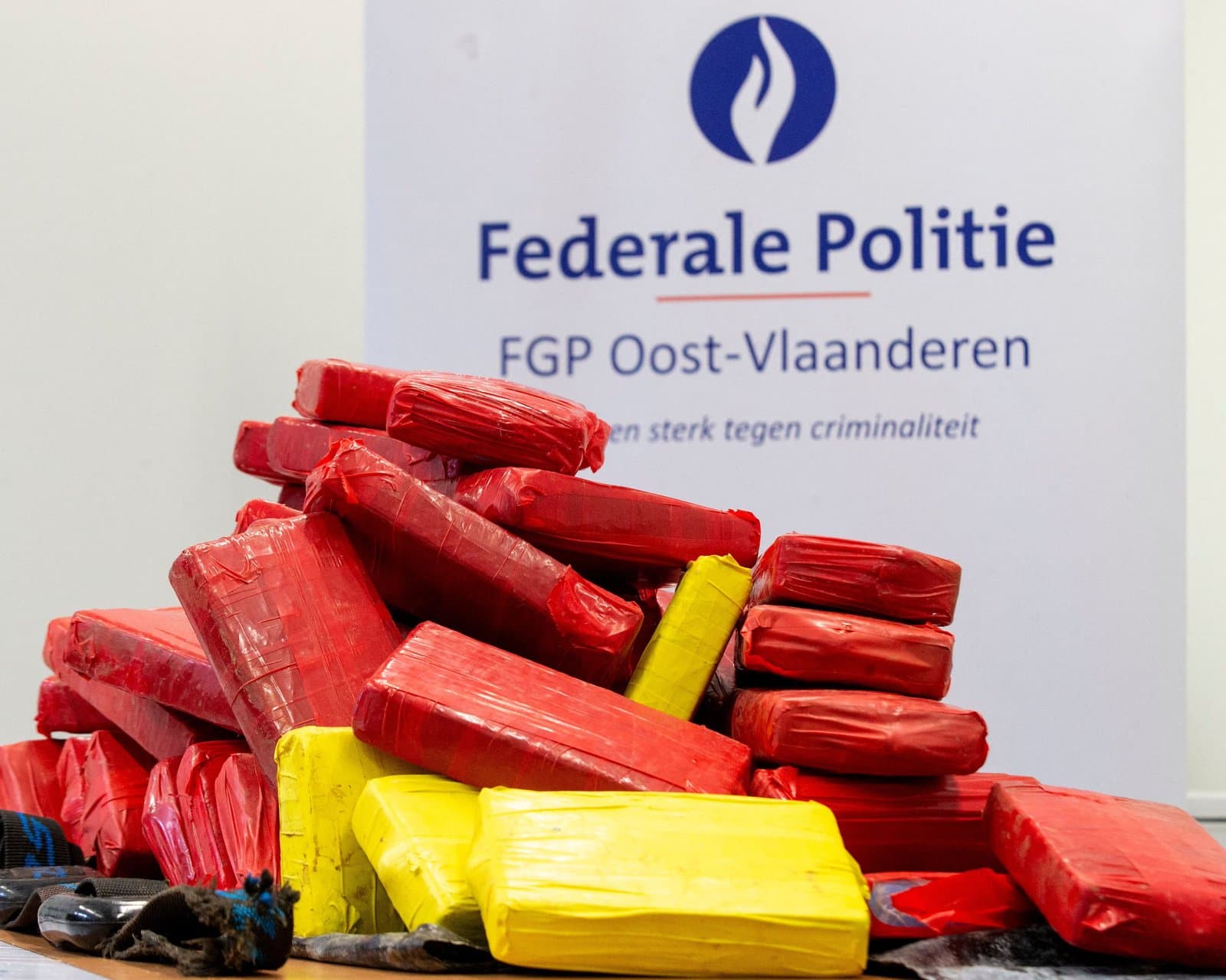 Packages of seized cocaine piled on a table in front of a Belgian federal police East Flanders banner